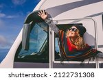 Overjoyed young adult woman oustretching arms outside the windows of a camper van and celebrate freedom and summer holiday travel vacation lifestyle