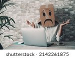 Small photo of Modern worker with carton sad box on head open arms with desolation gesture in front of a laptop. Online crypto smart working business job activity. Concept of fail and lost work. Bad day office