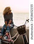 Small photo of People enjoying outdoor leisure actvity looking a beautiful coloured sunset - beautiful adult young woman with long curly blonde hair enjoy the relax after a bike tour - horizon and sun with ocean