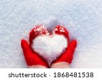 hands in knitted mittens with a heart made of snow on a winter day