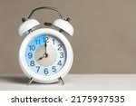 Small photo of Eight o'clock on the alarm. A white alarm clock is on a white table. The clock hand points to 8 o'clock. Time to change to summer or winter time. Set an alarm for 8:00 or 20:00. copy space