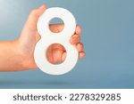 Small photo of Eight in hand. A hand holds a white number 8 on a blue background. Concept with number eight. Birthday 8 years, percentage, eighth grade or day, international women's day.