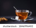 Small photo of A cup of tea, Cinnamon tea, Cinnamon drink with cinnamon stick on a Tea Bag, leaf on a Black background, Spoon, Transparent cup, Ceylon Tea, Sri lanka, Ceylon Cinnamon