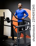 Small photo of An African man in sportswear runs on a curved treadmill inside a gym. Curvy treadmill concept. Running on manual treadmills.