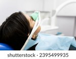Small photo of An adult woman sits in a dentist's clinic wearing a nasal mask to inhale nitrous oxide. Dentist fear concept. Feeling of relaxation with laughing gas.