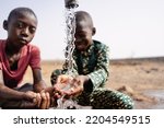 Two African toddlers playing with the water that flows from a rural faucet on the outskirts of their village; concept of water scarcity
