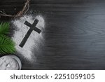Small photo of Border of cross of ashes, crown of thorns, palm leaves and bowl of ashes on a dark wood background with copy space