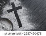 Small photo of Cross of ashes and bowl filled with ashes on a dark wood background with copy space