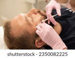 Small photo of Men's cosmetology. Cosmetologist makes botulinum toxin beauty injection procedure to man in wrinkles near eyes of rejuvenation of handsome young man with beard in beauty salon.