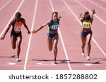 Small photo of Female sprinters crossing the finish line at the end of a sprint race on a bright, sunny day at the track