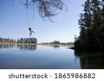 Horizontal shot of a young man swinging off a rope above the lake on a sunny day with copy space.