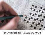 Small photo of Close up hand holding pencil over crossword puzzle on newspaper. Game on for writing some letters to solve and completing the empty table.