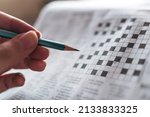 Small photo of Close up hand holding pencil over crossword puzzle on newspaper. Game on for writing some letters to solve and completing the empty table. Focus on empty crossword table.