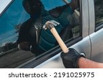 Small photo of Robber man in mask with a hammer breaks the car door window. The concept of robbery or auto theft.