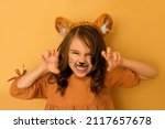 Small photo of A curly-haired brunette girl with a tiger's rim and ears and a painted face growls, showing her teeth and making a gesture with her hands. The Year of the Tiger according to the Eastern calendar