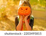 The child covers his face with a carved pumpkin with a fearsome terrifying look. Dressing up for Halloween.