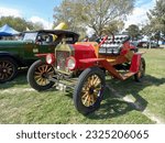 Small photo of Chascomus, Argentina - Apr 15, 2023: Old red 1915 Ford Model T open runabout roadster on the lawn. Nature, green, grass and trees. Classic car show.
