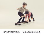 Portrait of playful little boys, children in retro checkered shirts playing together, skateboarding, having fun isolated over grey background. Concept of childhood, friendship, fun, lifestyle, fashion