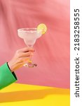 Female hand holding glass of delicious margarita cocktail isolated over pink yellow background. Cheers. Concept of cocktails, alcoholic drinks, taste, party, mix. Copy space for ad. Retro style