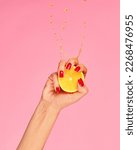 Small photo of Vitamines. Female hand with bright manicure squeezes half of orange over pink background. Pop art food photography. Drops of juice fly up. Concept of healthy eating, art, fashion, creativity and ad