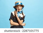 Small photo of Gossip, tattle. One charming little girl wearing vintage dress and hat looking holding hand near mouth and whispers over blue background. Vintage, retro, uniqueness, art, childhood, ad concept