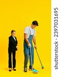 Small photo of finicky manager, little girl, schoolgirl tells janitor where on floor to pick up dust on floor against vivid yellow background. Concept of business, office, work, job, occupation, finance, management.