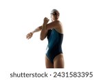 Young, athletic woman in swimwear stretching arms, training before swimming race against white studio background. Concept of professional sport, motion, strength and power. Ad