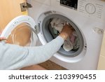 Woman's arm filling the washing machine drum. Concept of energy consumption, high price of electricity, household chores, housewives, turning on the washing machine.