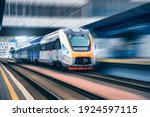 High speed train in motion on the railway station at sunset. Modern intercity passenger train with motion blur effect on the railway platform. Industrial. Railroad in Europe. Transportation. Industry
