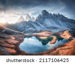 Aerial view of beautiful rocks, mountain lake, reflection in water and houses on the hill at sunset. Summer landscape with mountains, blue sky and sunlight. Dolomites, Italy. Top view of Italian alps