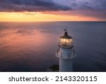 Lighthouse on the mountain peak at colorful sunset in summer. Aerial view. Beautiful lighthouse, light, sea and orange sky with purple clouds at night. Top view of Cape Lefkada, Greece. Landscape