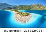 Small photo of Aerial view of sea bay, sandy beach with umbrellas, trees, mountain at sunny day in summer. Blue lagoon in Oludeniz, Turkey. Tropical landscape with island, white sandy bank, blue water. Top view