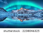 Northern lights over the snowy mountains, sea coast, reflection in water at night in Lofoten, Norway. Aurora borealis and snow covered rocks. Winter landscape with polar lights and fjord. Starry sky