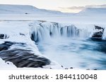 Slow shutter of the beautiful Goðafoss Waterfall in the north of Iceland at sunset during the winter with snow and ice surrounding the waterfall