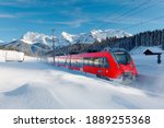 Small photo of A local train traveling by a forest in a valley covered by deep snow on a sunny winter day and Karwendel Mountain dominating the background under blue sky near Garmisch-Partenkirchen, Bavaria, Germany