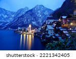 Scenery of Hallstatt (a lakeside village in Salzkammergut area of Austria) on a peaceful winter morning, with reflections of lights in the water and snow on the rugger mountainside at blue twilight