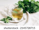 nettle tea. a cup with nettle tea next to a bunch of fresh nettles on a light background. medical herbal tea.