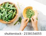 Green pea pods. female hands hold a pod of peas and cleans its wooden bowl on a white background. harvesting concept. healthy vegetables.