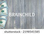 Small photo of BRAINCHILD - word (text) on wooden background, money, dollars. Business concept (copy space).