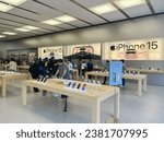 Small photo of DALLAS, TX, US-OCT 28, 2023: Large iPhone 15 wall poster and customer shopping for latest models on wooden table display at Apple Store in downtown, chain of retail stores owned operated by Apple Inc