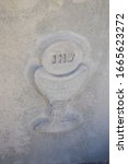 Small photo of Stylized image engraved in stone of a pyx with a host upon it, bearing the IHS Christogram