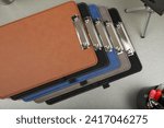 Small photo of Colorful leather clipboard. Genuine leather clipboard, concept shot, top view, different color, clamshell and stitched clipboard