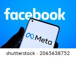 Small photo of META company logo seen on smartphone hold in hand and blurred Facebook logo on background screen. New Facebook company logotype for METAVERSE. Stafford, United Kingdom, October 28, 2021.