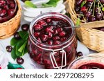 Small photo of Cooked homemade cherry jam in glass jar on white wooden table outdoors, fresh cherry jam close up, food and healthy eating concept
