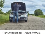 Worried man holding his head by hands standing near his old broken car with raised hood on the road                               