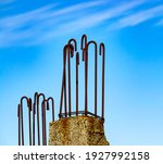 Small photo of Rusty, metal hooks on top of a concrete, steel reinforced beam, have been abandoned decades ago, as the building project faltered, and now simply stick out against the backdrop of a cloudy, blue sky.