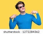 Small photo of Young man wearing funny thug life glasses over isolated background looking confident with smile on face, pointing oneself with fingers proud and happy.