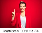 Young beautiful business woman standing over red isolated background showing and pointing up with finger number one while smiling confident and happy.