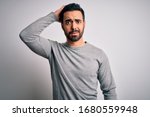 Young handsome man with beard wearing casual sweater standing over white background confuse and wonder about question. Uncertain with doubt, thinking with hand on head. Pensive concept.