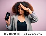 Young african american woman with afro hair holding cracked and broken smartphone screen stressed with hand on head, shocked with shame and surprise face, angry and frustrated. Fear and upset